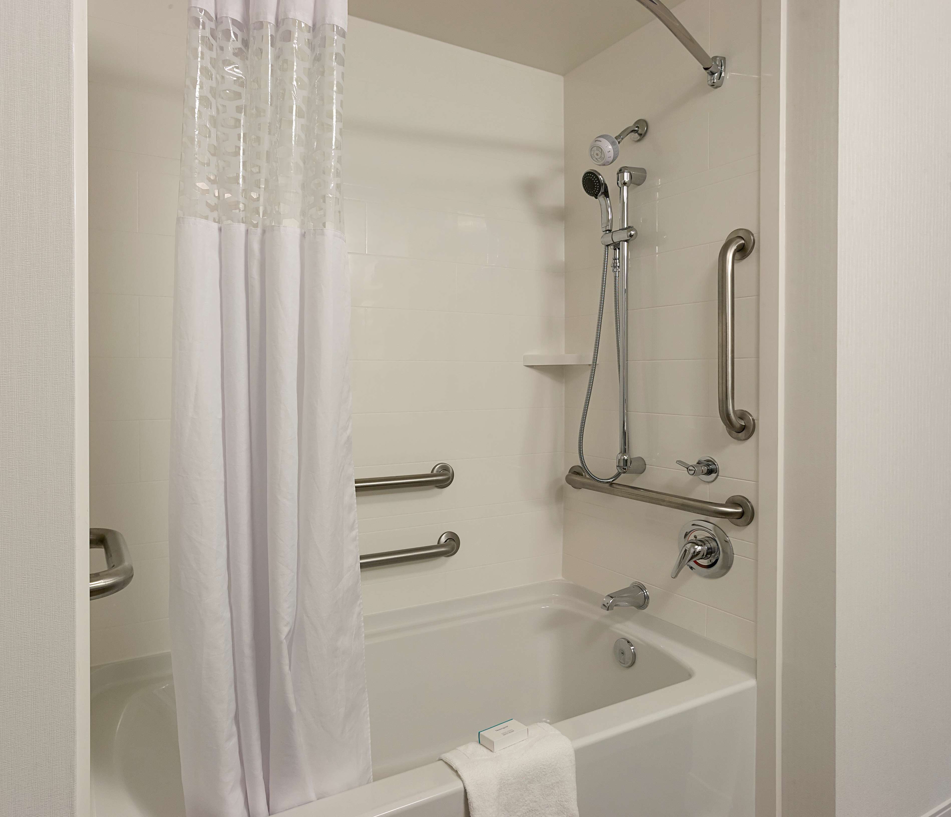 Ein modernes Badezimmer mit Badewanne, Dusche und Haltegriffen.