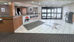 A BISON Inn & Suites reception area with a wooden reception desk, a large sign, a clock, and an ATM. - Bison Inn & Suites on University (Fargo)