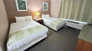A hotel room with two beds, a nightstand with a lamp, a window with curtains, and an air conditioning unit. - Bison Inn & Suites on University (Fargo)