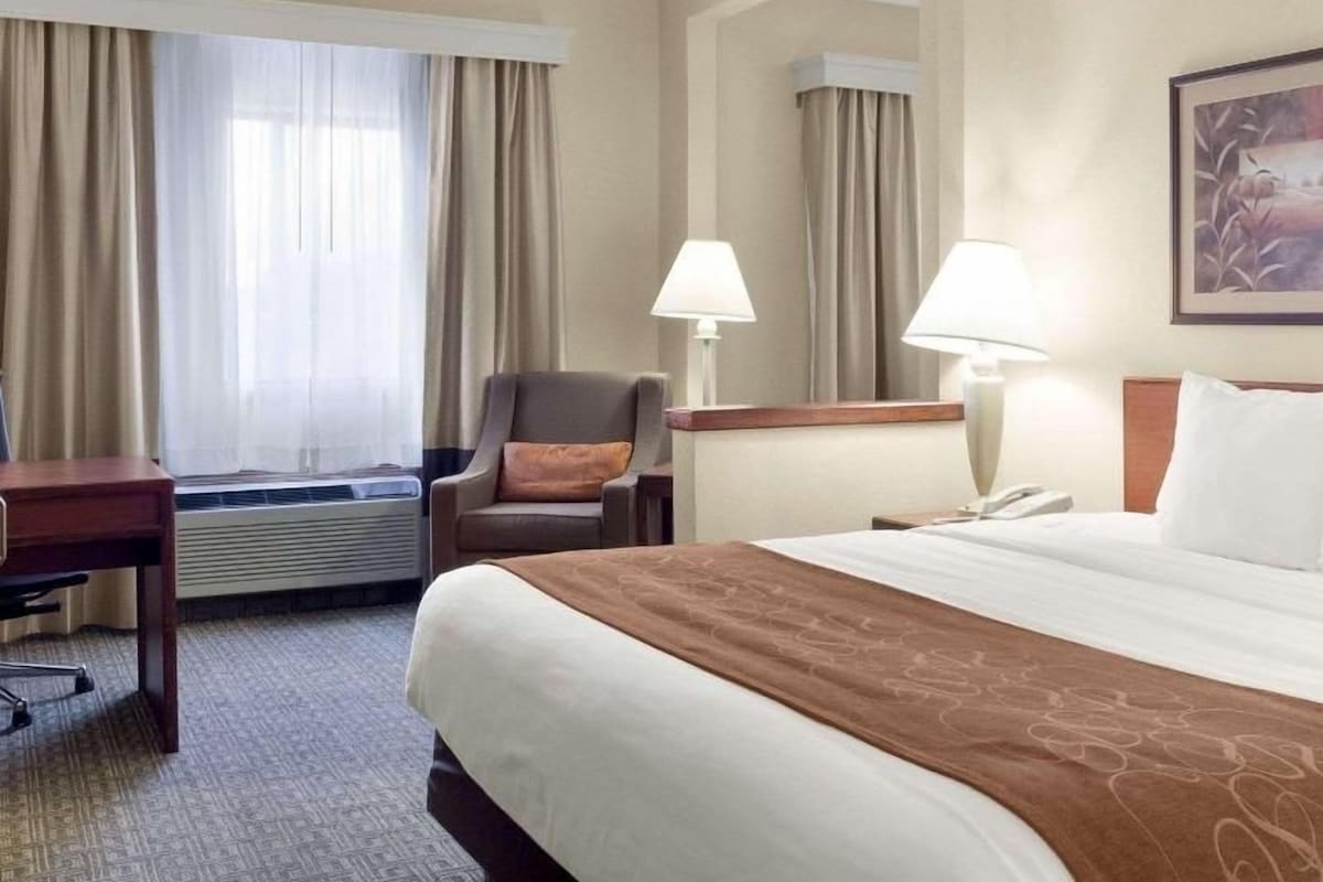 A hotel room with a bed, a desk, a chair, a lamp, and a window with curtains.