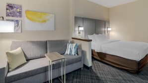 A hotel room with a grey sofa, a small table, a bed with white bedding, and two wall-mounted lamps. - Comfort Inn Bismarck (Bismarck)