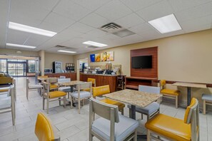 A dining area with tables and chairs, a kitchen area, and a television mounted on the wall. - Comfort Inn Bismarck (Bismarck)