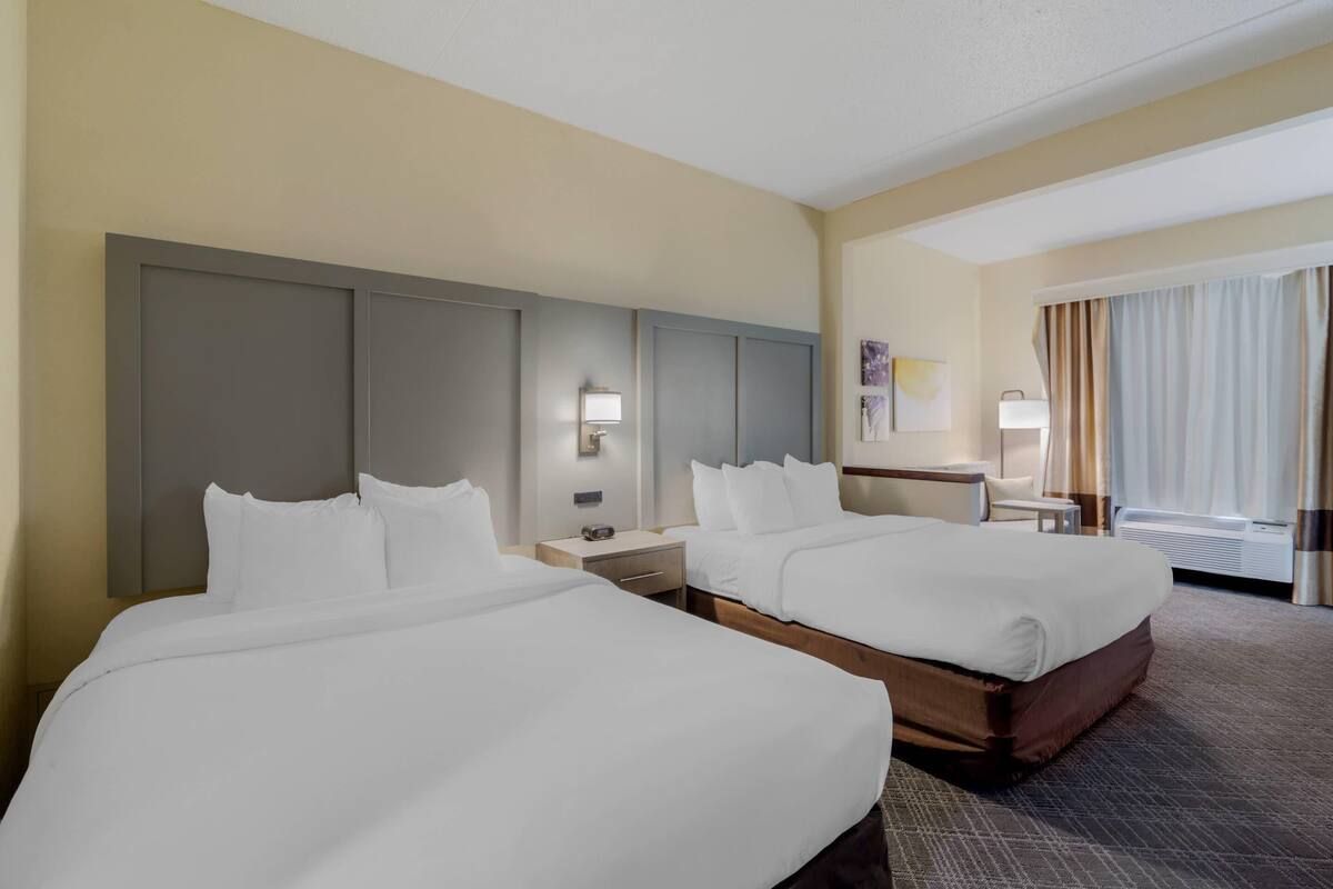 A hotel room with two beds, a desk, a chair, a lamp, and a window with curtains.