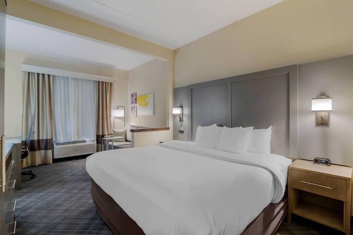 A hotel room with a large bed, bedside tables, a desk, a chair, and a window with curtains.