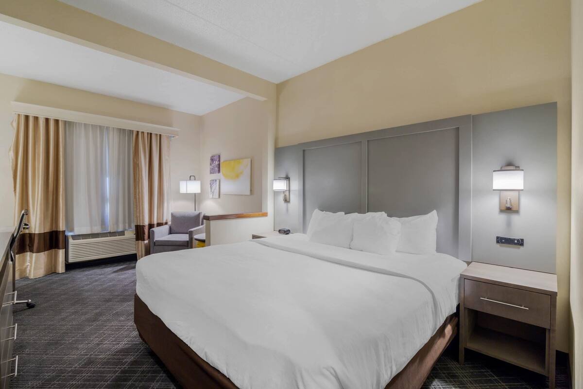 A hotel room with a large bed, a desk, a chair, and a nightstand.
