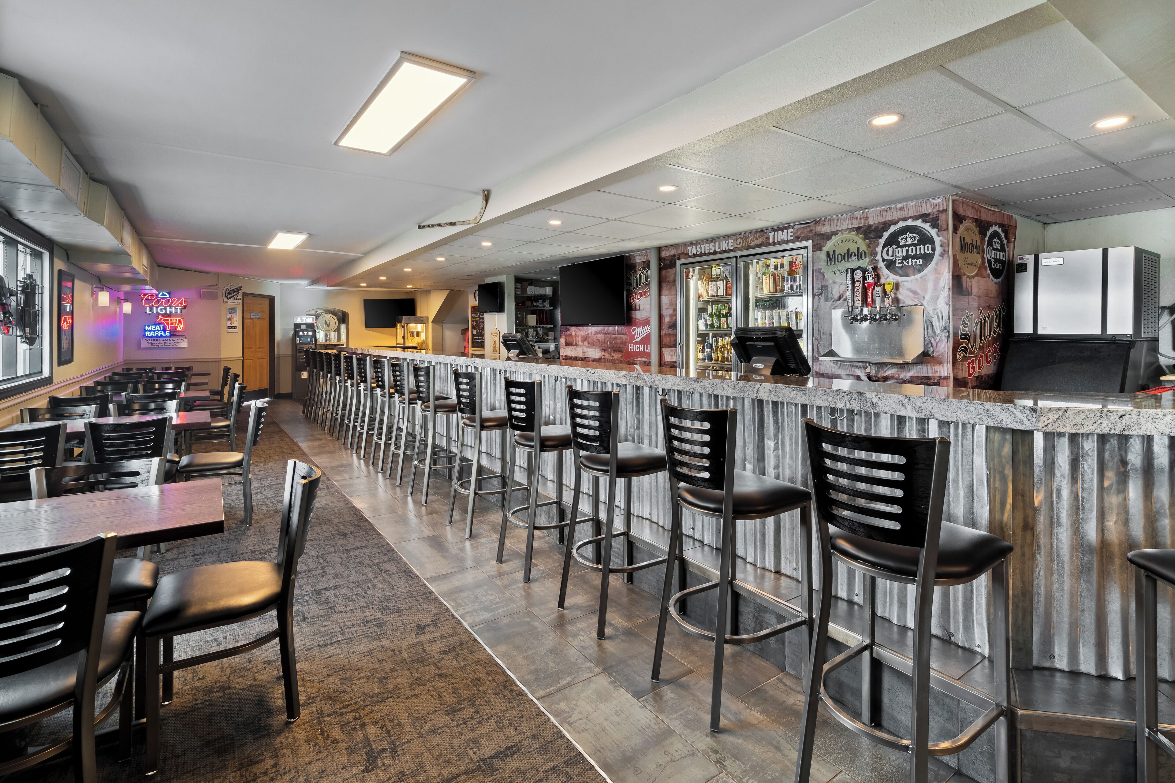 Een bar met een lange toonbank, barstoelen en een koelkast vol drank.