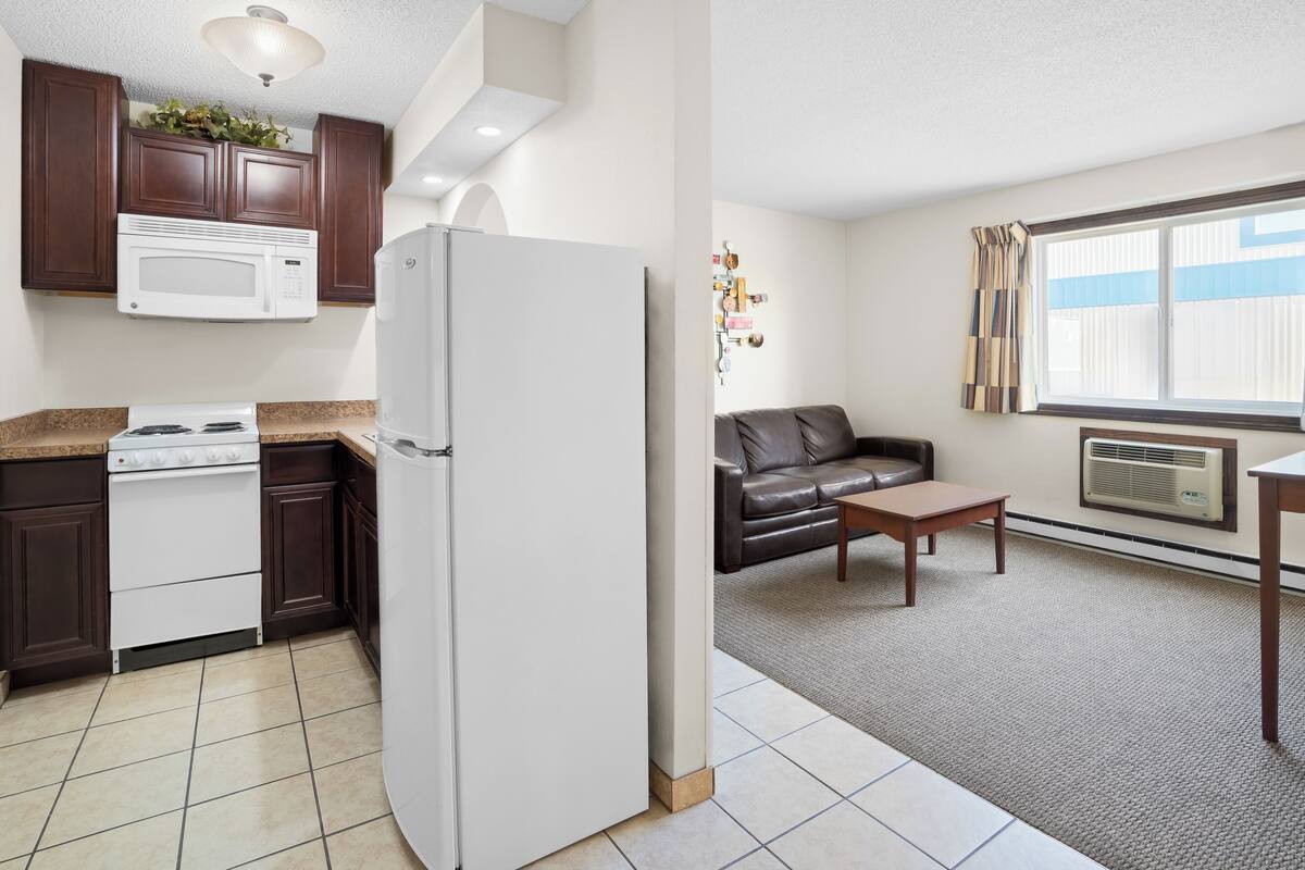 A kitchen with a stove, microwave, and refrigerator, and a living area with a couch, table, and window.