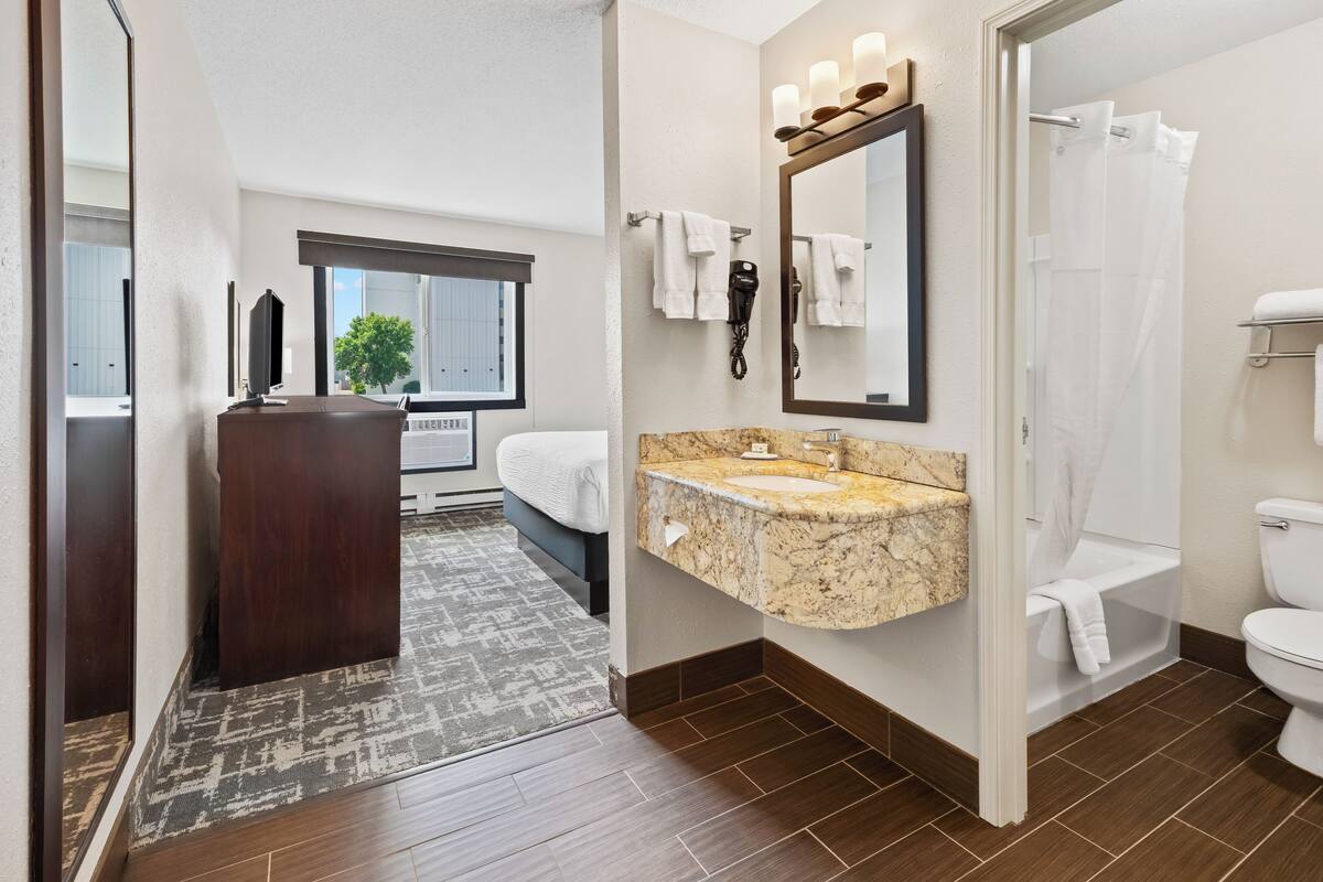 A modern bathroom with a marble sink, a large mirror, a hairdryer, and a shower curtain.