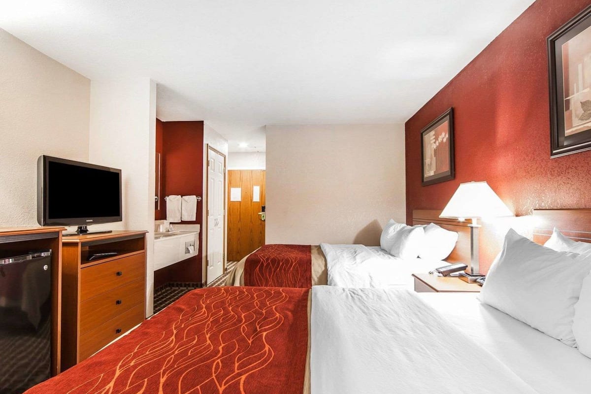 A hotel room with two beds, a desk with a television, a dresser, and a bathroom visible through an open door.
