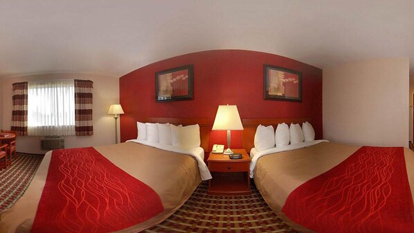 Habitación de hotel con dos camas, un escritorio, una silla, una lámpara y dos cuadros en la pared.