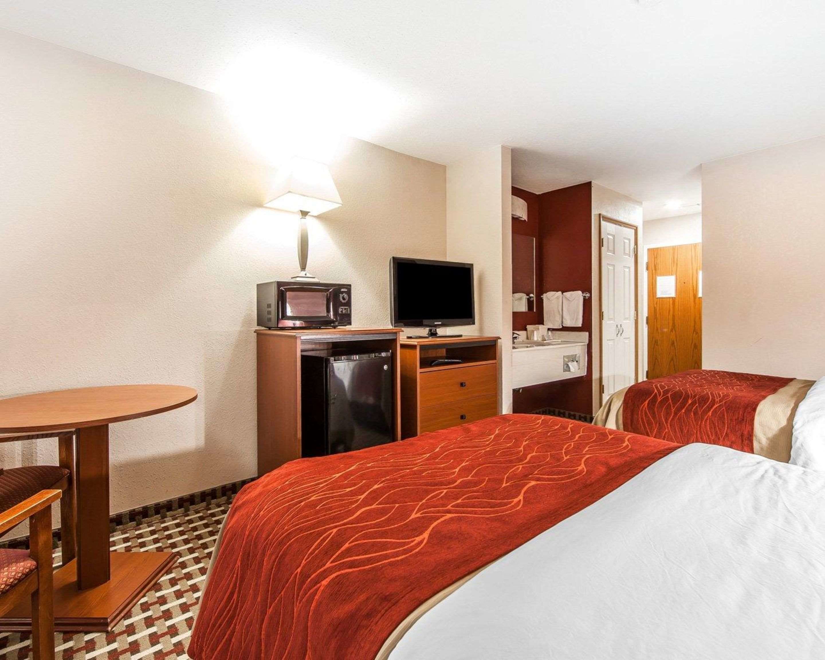 Camera d'albergo con due letti, una scrivania con forno a microonde, televisione, piccolo frigorifero e bagno con specchio e porta asciugamani.