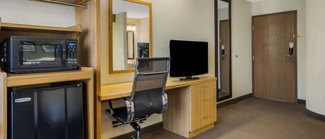 A hotel room with a kitchenette, a desk with a computer, a chair, and a wardrobe.