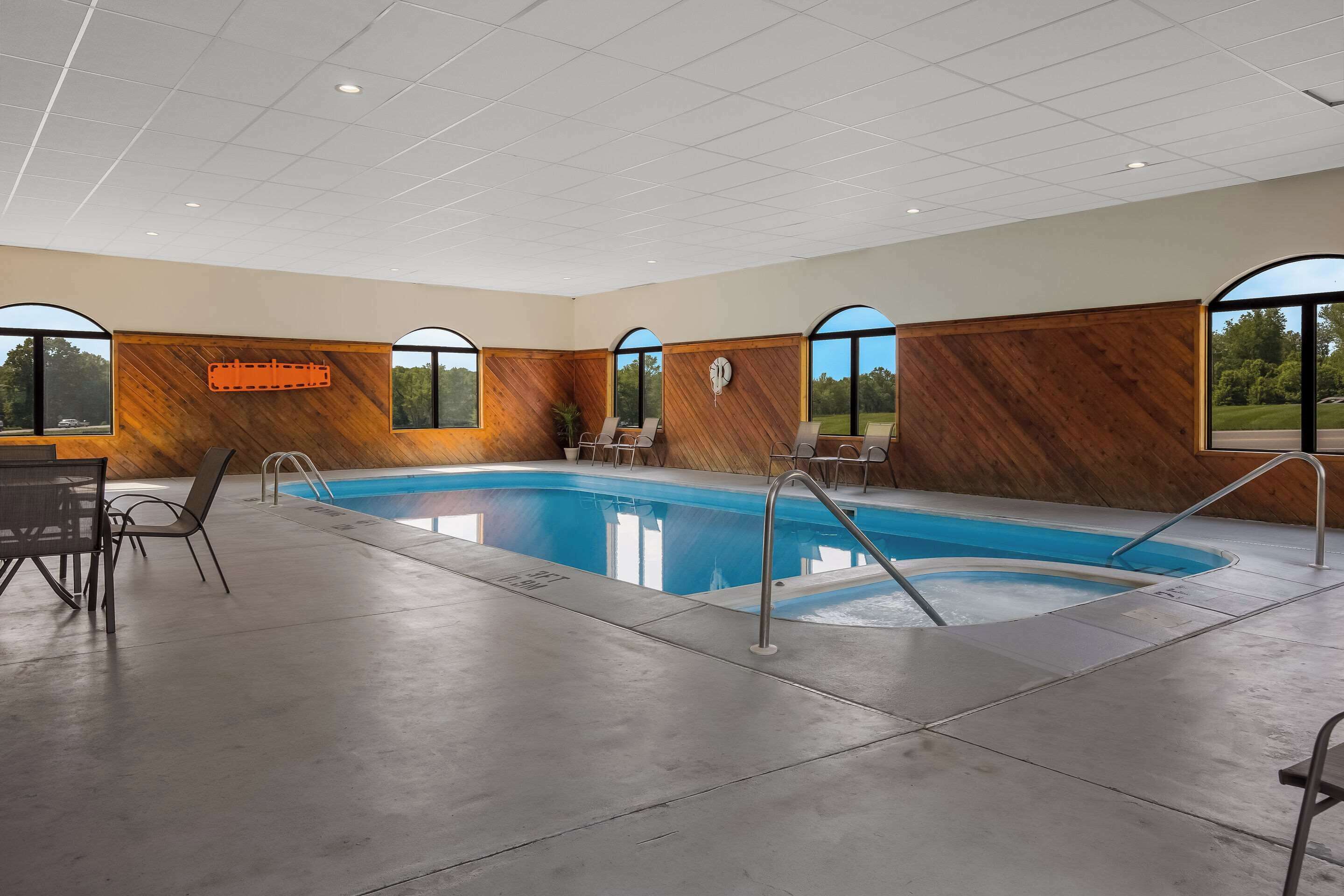 Un área interior de piscina moderna con una pared de madera, piscina y zona de estar con sillas.