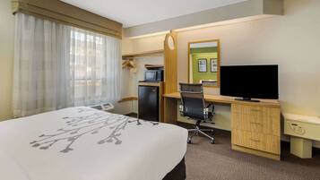 Ein Hotelzimmer mit einem Bett, einem Schreibtisch mit Computer, einem Fernseher und einer Mikrowelle.