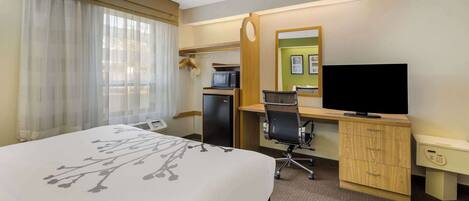 Habitación de hotel con cama, escritorio con computadora, televisor y microondas.