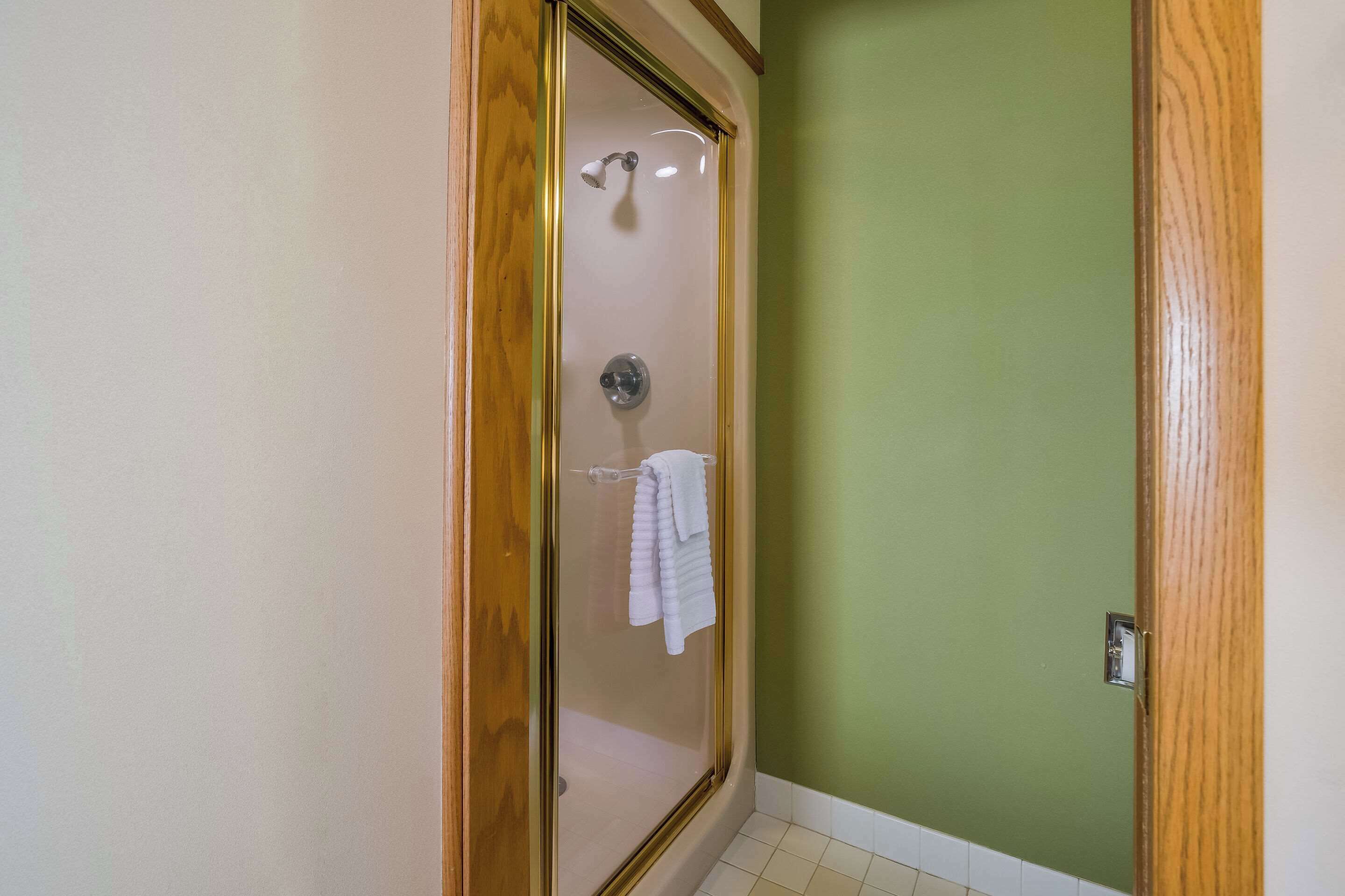A shower with a glass door, a towel rack with a folded towel, and a green wall.