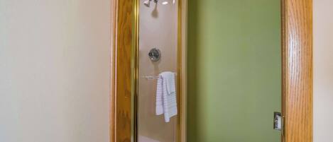 A shower with a glass door, a towel rack with a folded towel, and a green wall.