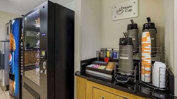 A self-service beverage station with a refrigerator, coffee machines, and a trash bin.