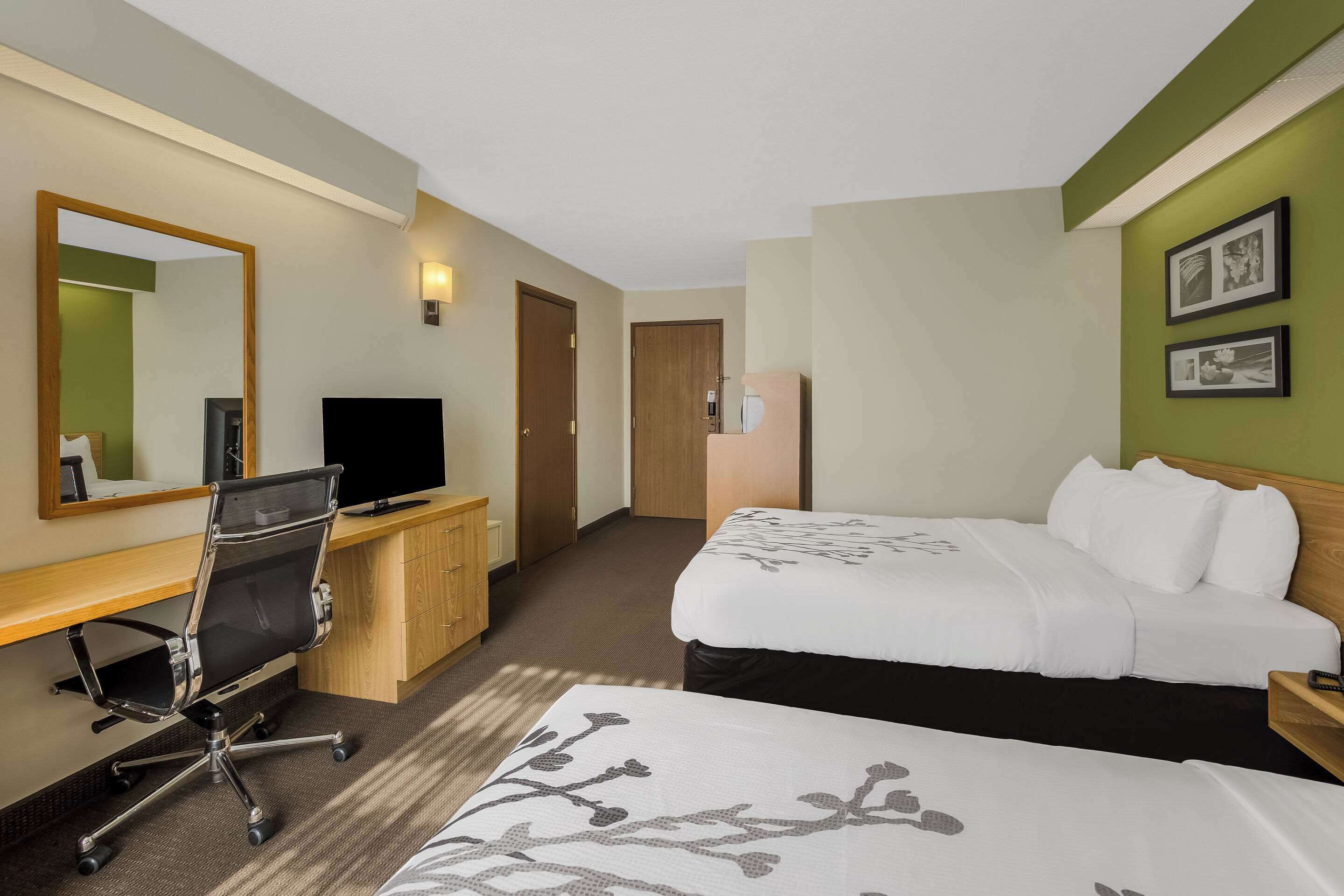 A hotel room with two beds, a desk with a computer, a chair, a TV, and a mirror.