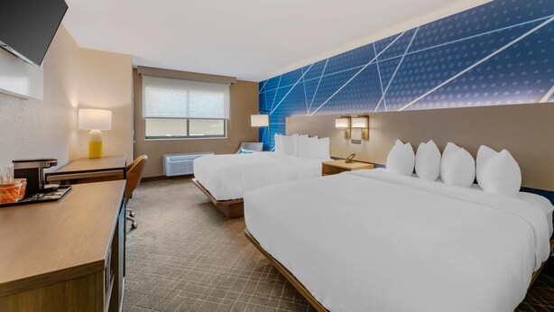 A hotel room with two beds, a desk, a chair, a flat-screen TV, and a window with blinds.
