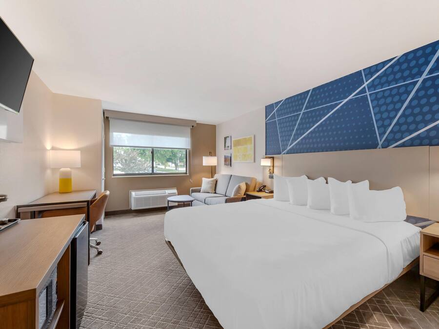 Una habitación de hotel con una cama grande, un escritorio, una silla, una mesita y un ventanal.