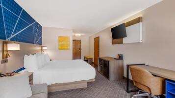 A hotel room with a bed, a desk, a chair, a TV, and a wall-mounted TV.