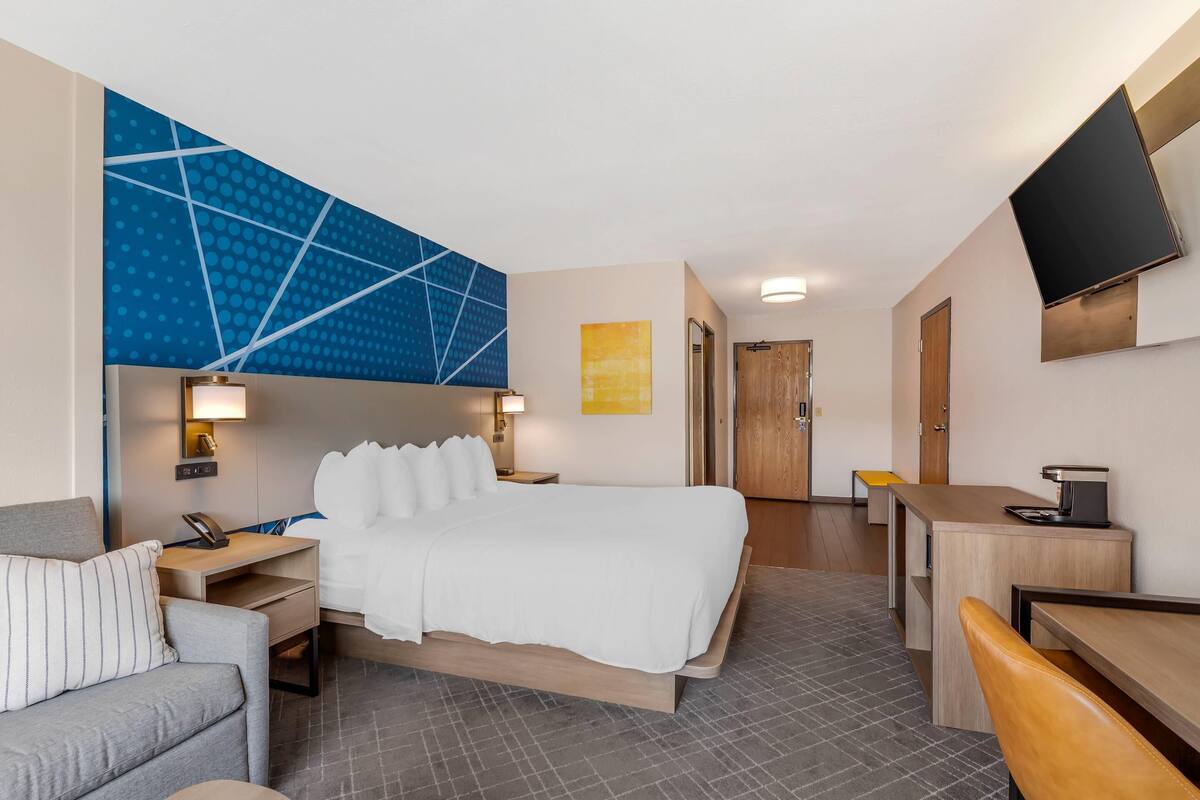 Habitación de hotel con cama, escritorio, silla, sofá, televisor y puerta del baño.