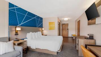 Quarto de hotel com cama, escrivaninha, cadeira, sofá, televisão e porta de banheiro.