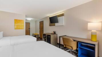 Une chambre d’hôtel avec deux lits, un bureau avec une chaise, un téléviseur fixé au mur et une lampe sur une table de chevet.