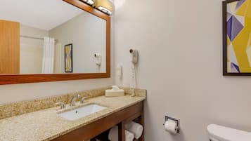A bathroom with a granite countertop sink, a mirror, a towel rack, a toilet, and a hairdryer on the wall.