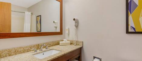 A bathroom with a granite countertop sink, a mirror, a towel rack, a toilet, and a hairdryer on the wall.