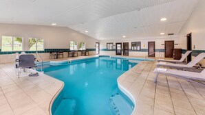 A swimming pool with a lifeguard chair and lounge chairs, surrounded by tiled walls and windows.