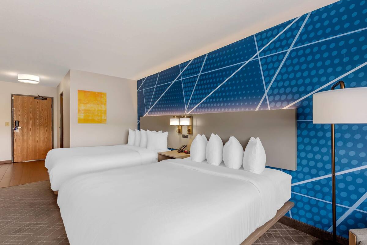 Habitación de hotel con dos camas, una puerta de madera, una pared con diseño de puntos azules y una lámpara.