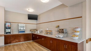 A modern kitchen with wooden cabinets, a countertop with various appliances, and a flat-screen TV mounted on the wall.