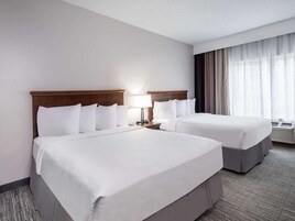 Habitación de hotel con dos camas, una mesita de noche con lámpara, una ventana con cortinas y un equipo de aire acondicionado.