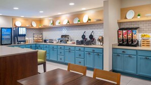 A modern kitchen with blue cabinets, a coffee machine, waffle maker, and a cereal dispenser.