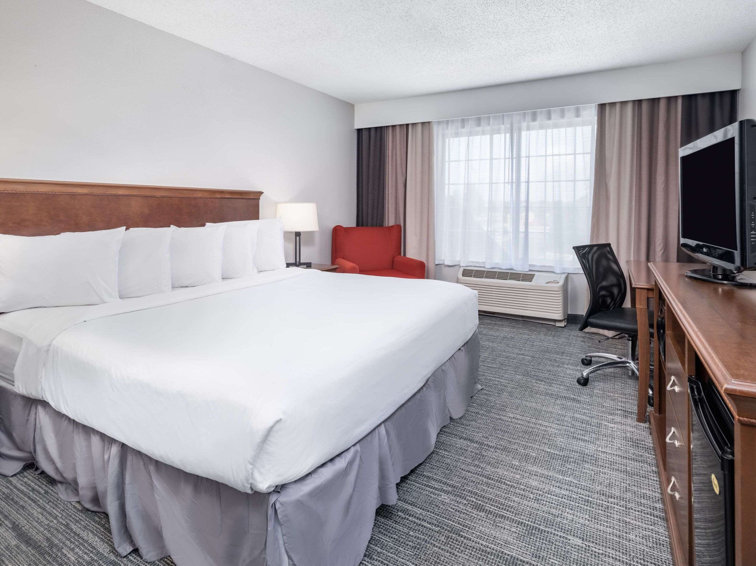 Habitación de hotel con una cama grande, un escritorio con computadora, un televisor y una silla.