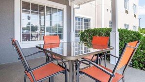 A covered patio with a glass table and four orange chairs.