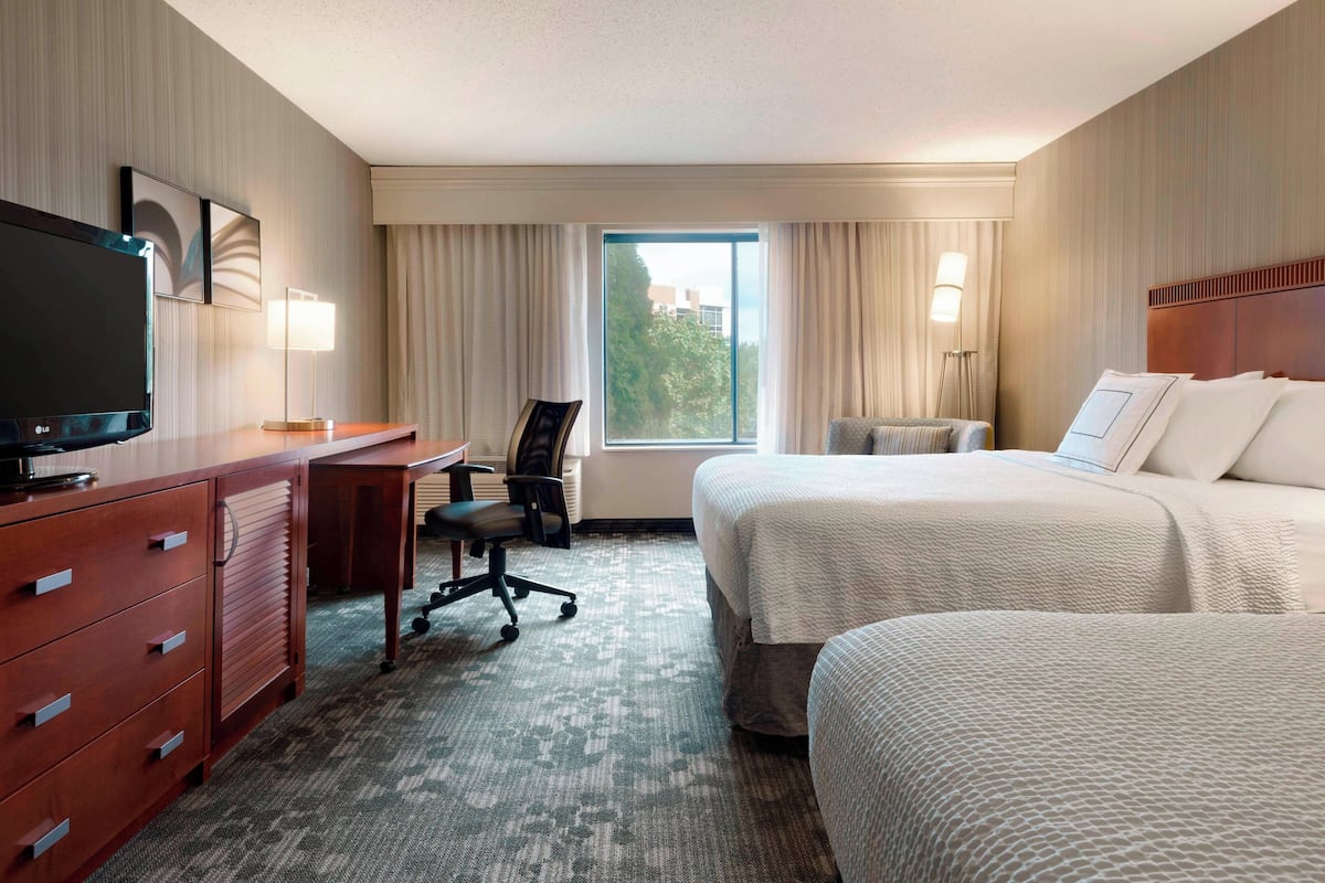 A hotel room with a bed, a desk, a TV, and a window with curtains.