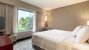 A hotel room with a large bed, a desk with a computer, a chair, and a window with curtains.
