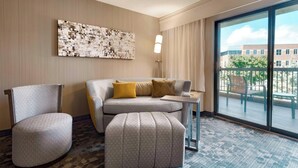 A hotel room with a grey sofa, a matching armchair, a small ottoman, a side table, and a large window offering a view of the outdoors. - Courtyard by Marriott Akron Fairlawn (Akron)