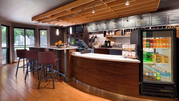 A modern bar area with a wooden counter, bar stools, a refrigerator stocked with beverages, and a menu board above the counter. - Courtyard by Marriott Akron Fairlawn (Akron)