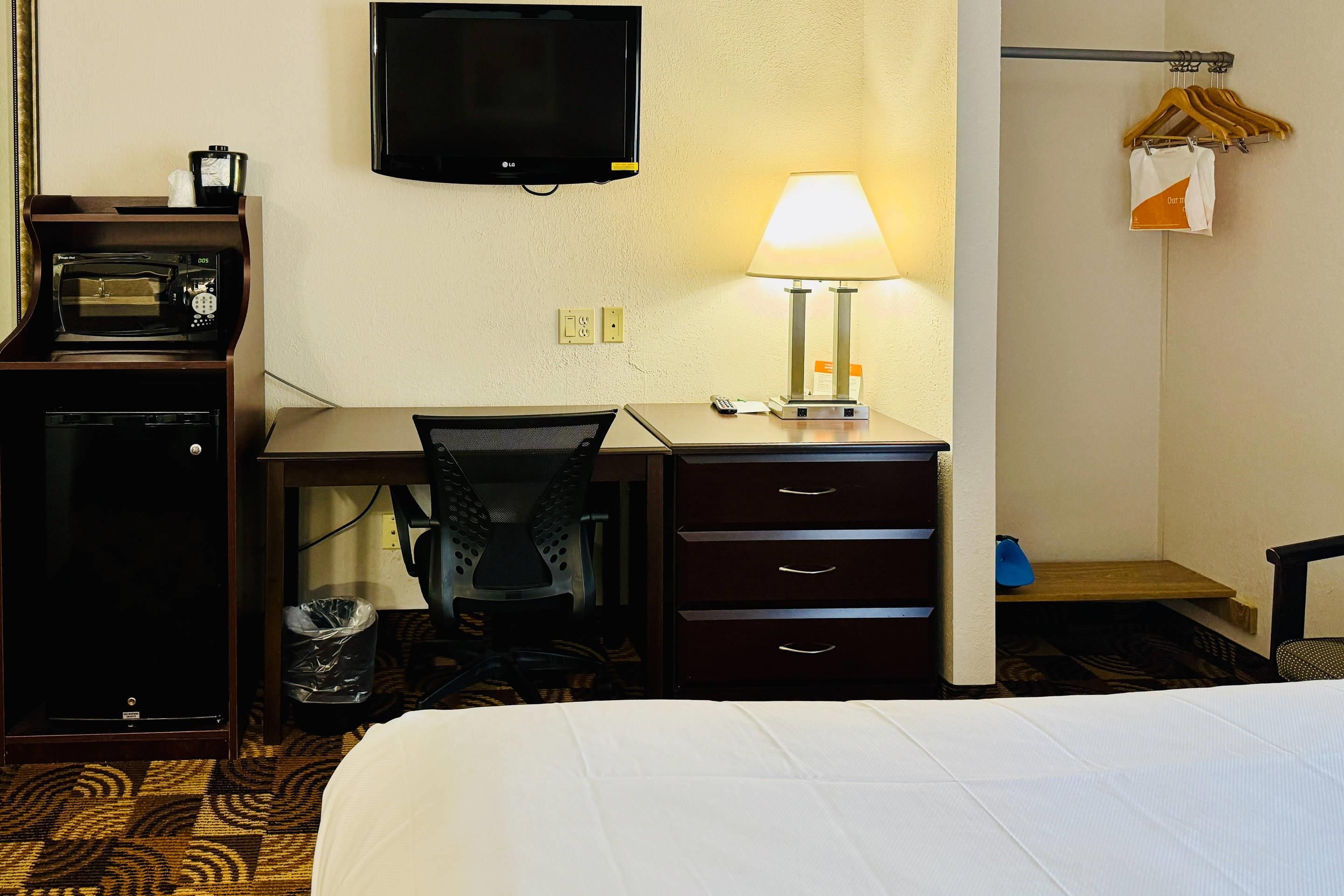 A hotel room with a bed, a desk with a lamp, a television, and a microwave.