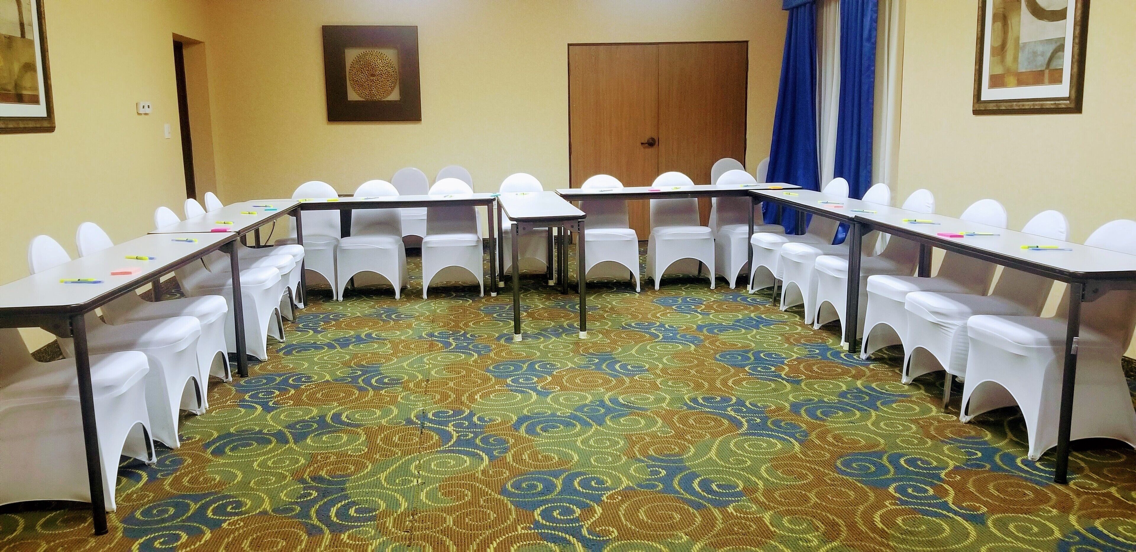 Una sala conferenze con una moquette fantasia, sedie bianche e tavoli disposti per riunioni.