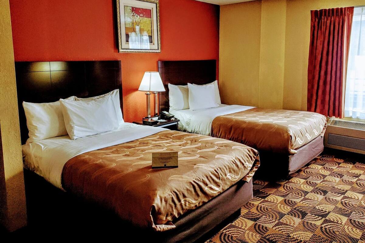 A hotel room with two beds, a nightstand, a lamp, a framed picture on the wall, and a window with curtains.