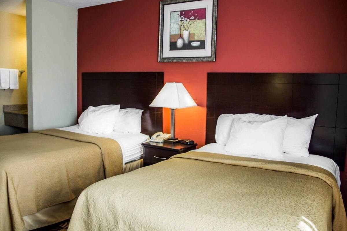 A hotel room with two beds, a nightstand with a lamp, a telephone, and a framed picture on the wall.