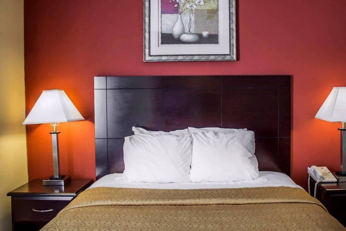 A hotel room with a large bed, two bedside lamps, a framed artwork above the bed, and a telephone on the nightstand.