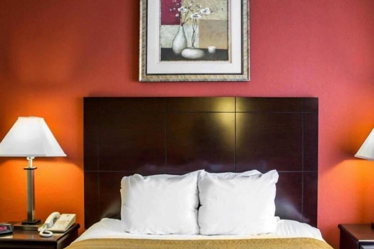 A hotel room with a large bed, two bedside tables, a nightstand, a framed picture on the wall, and a red wall.