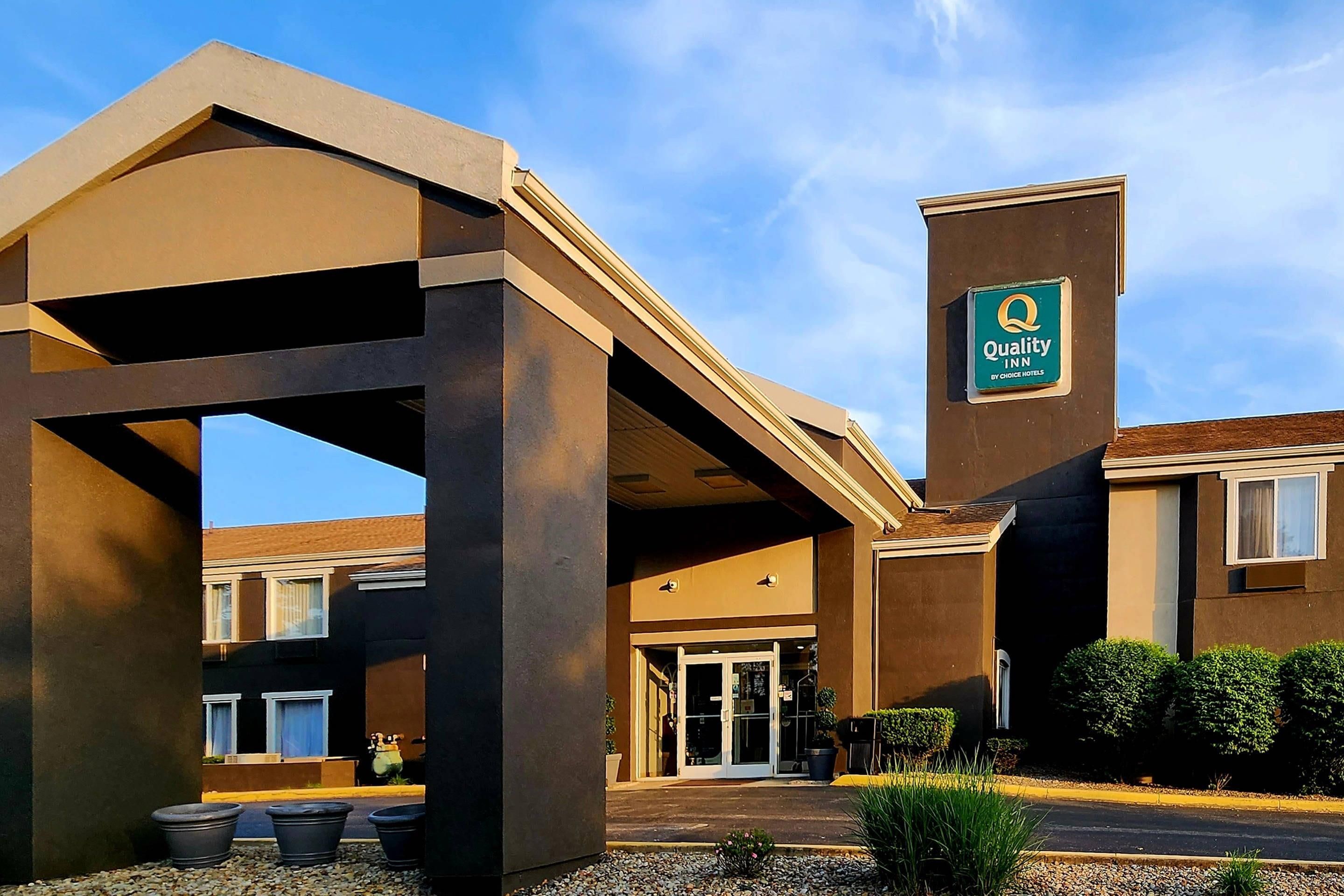 A hotel entrance with a covered walkway, a sign for Quality Inn, and a clear sky.