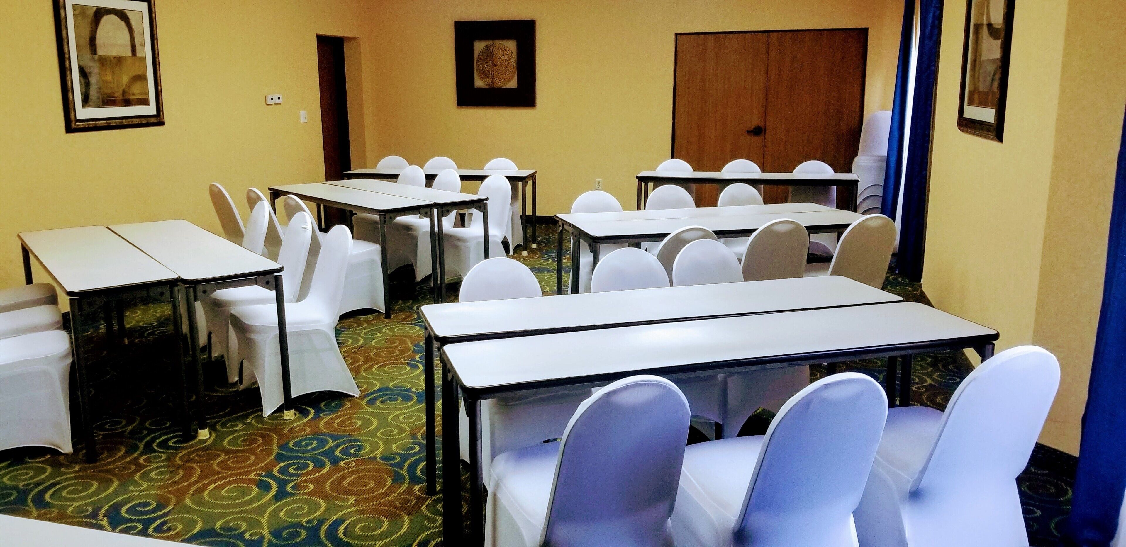 Uma sala de conferências com várias mesas e cadeiras, um tapete estampado e quadros decorativos nas paredes.
